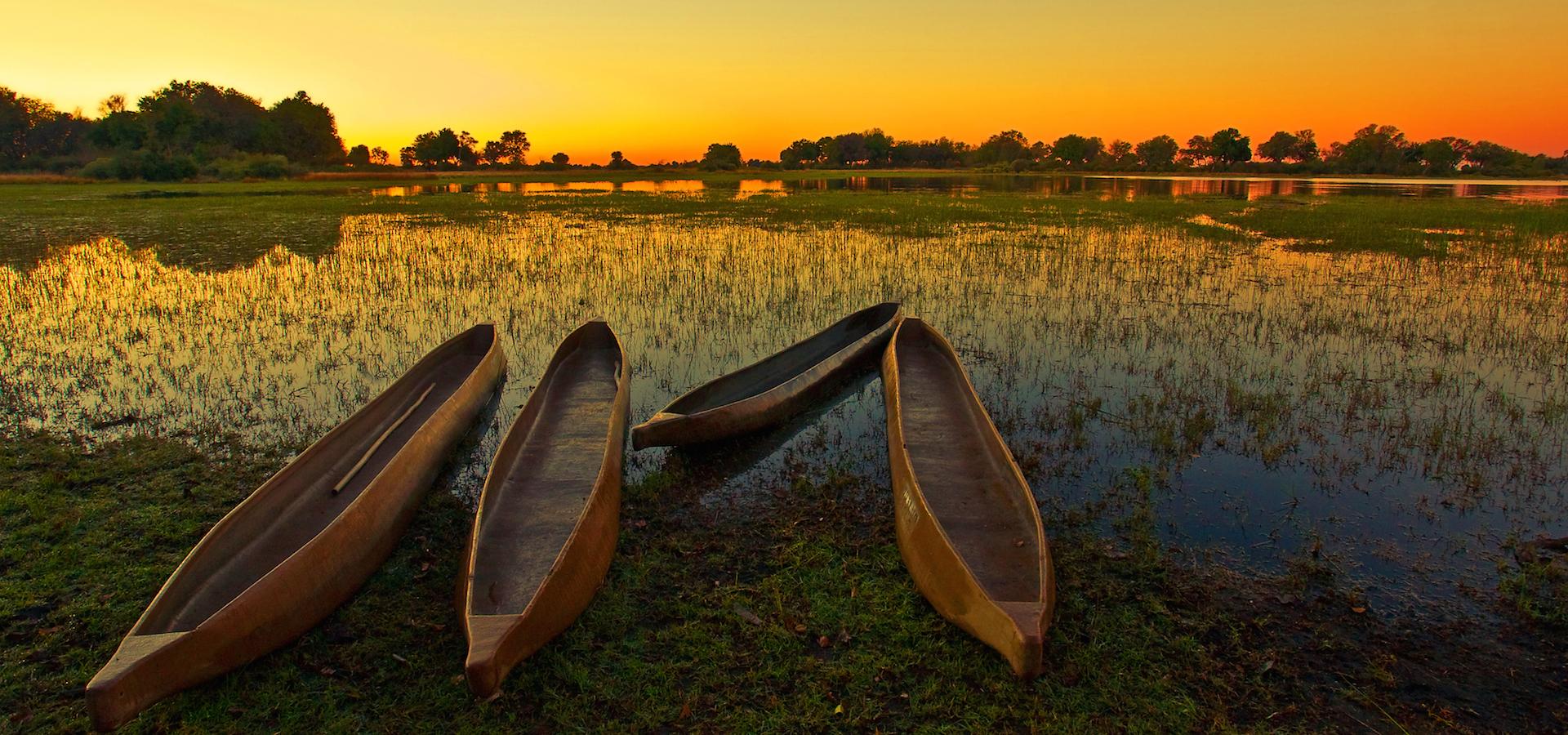 Sonnenaufgang im Okavango Delta: Im Vordergrund drei Mokoro, das klassische Fortbewegungsmittel im größten Binnendelta der Welt